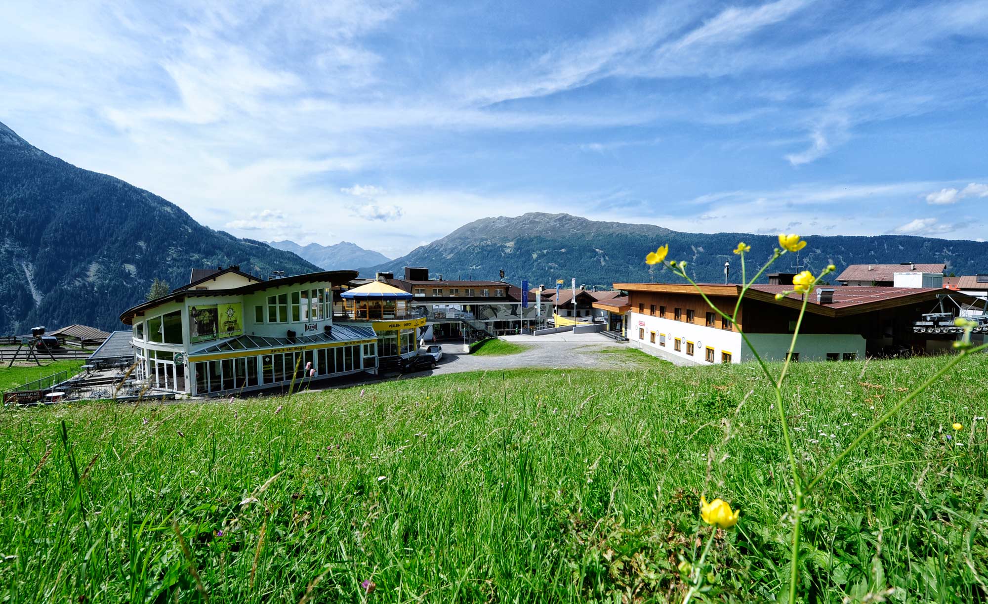 Das Gebäude von Sport Lentsch umgeben von Wiese und Berglandschaft.