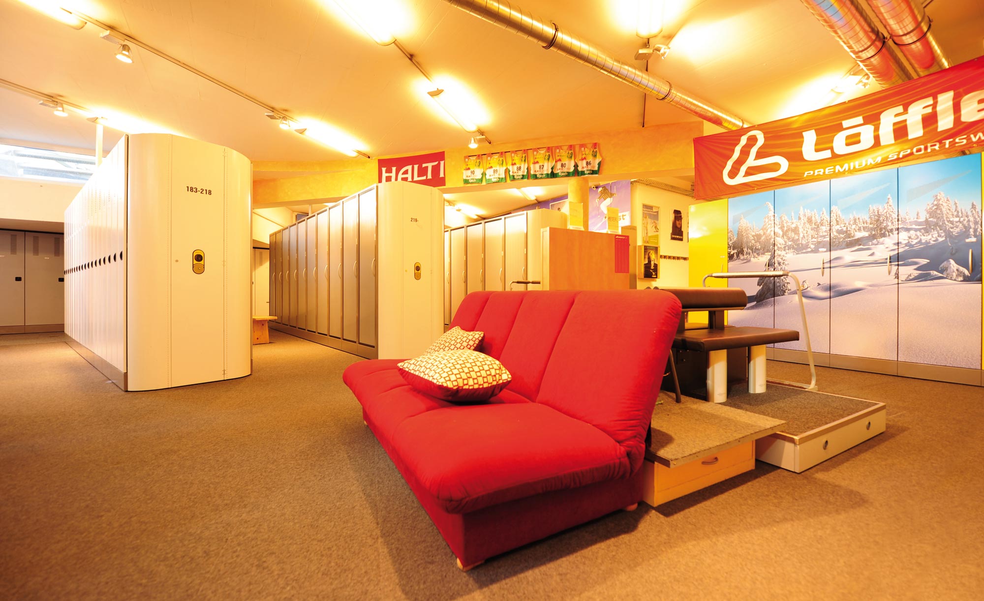 Gemütlicher Skidepotraum mit roten Sofa, Spinden und Werbebannern im Sportgeschäft Sport Lentsch in Jerzens.