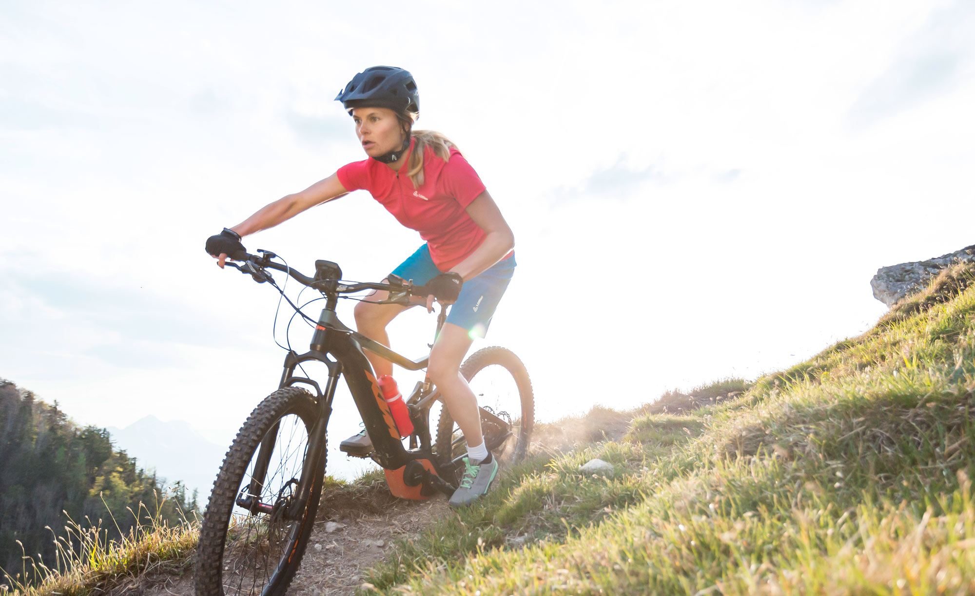 Eine Frau fährt mit ihrem Bike über einen Schotterweg, sie trägt Sportkleidung von der Marke Löffler.